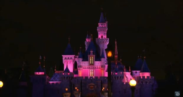 Sleeping Beauty Castle at Disneyland Resort glows in vibrant pink and purple hues under the night sky, creating an enchanting atmosphere for guests as part of Disney's reopening festivities.