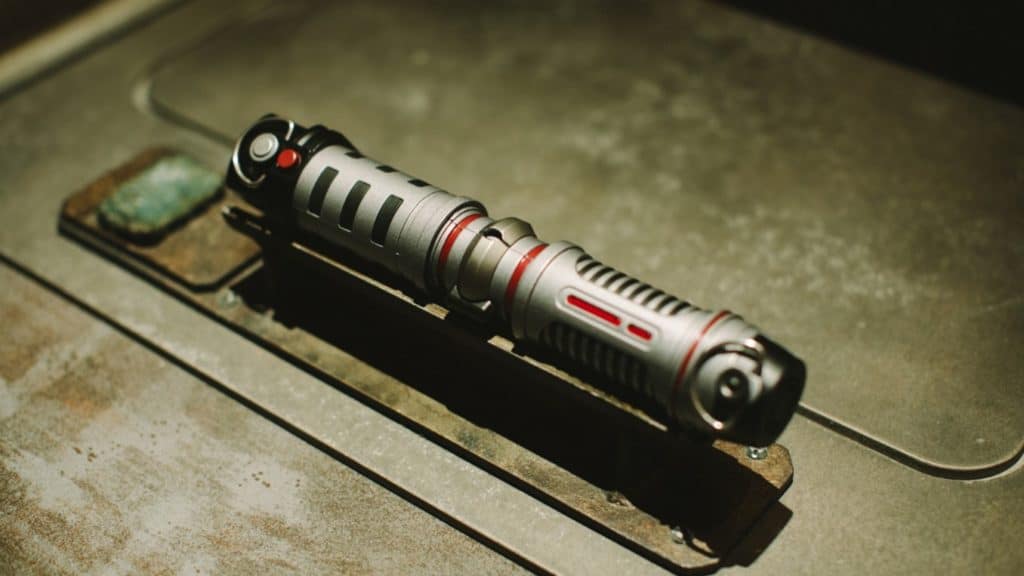 A custom Savi's Workshop lightsaber, with its metallic cylindrical design and futuristic details, displayed on a weathered metal workbench at Walt Disney World.