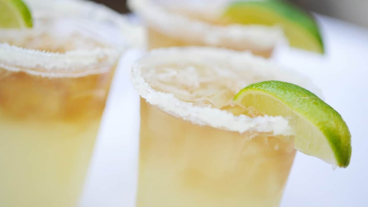 Three margarita glasses with salted rims, garnished with lime wedges and filled with ice, stand ready on a bright white table—the perfect way to toast the grand reopening of Disney’s BoardWalk at Joe’s Marvelous Margaritas.