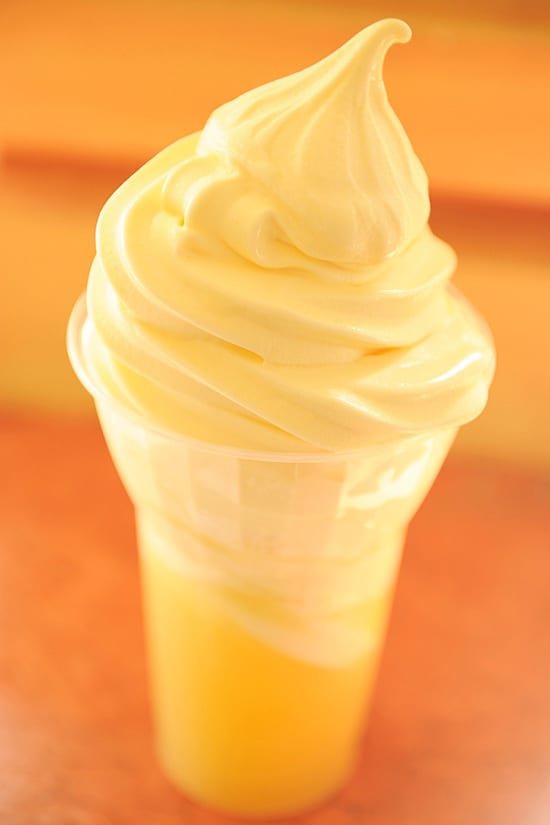 A cup of creamy yellow soft serve ice cream with a signature swirl on top, served in a clear plastic cup—an iconic Disney Parks treat, perfect for enjoying while you plan your next adventure or stream the latest Disney+ series.