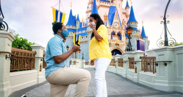 A magical proposal unfolds in front of Cinderella Castle at Walt Disney World, with both the future bride and groom wearing face masks—a memorable moment perfectly captured during their Disney PhotoPass session.