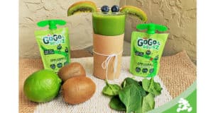 A vibrant green Grogu-inspired smoothie served in a clear glass with fresh kiwi and blueberries on top, surrounded by applesauce pouches, limes, spinach, and whole kiwis—perfect for Star Wars fans visiting a themed eatery or galactic café at a Disney park.
