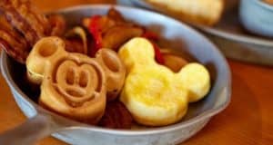 Mickey Mouse-shaped waffles with crispy bacon and golden potatoes are served in a metal pan atop a rustic wooden table—capturing the classic Disney breakfast just like you’d find at Whispering Canyon Café in Disney World, where Hidden Mickeys bring that extra touch of pixie dust to every bite.