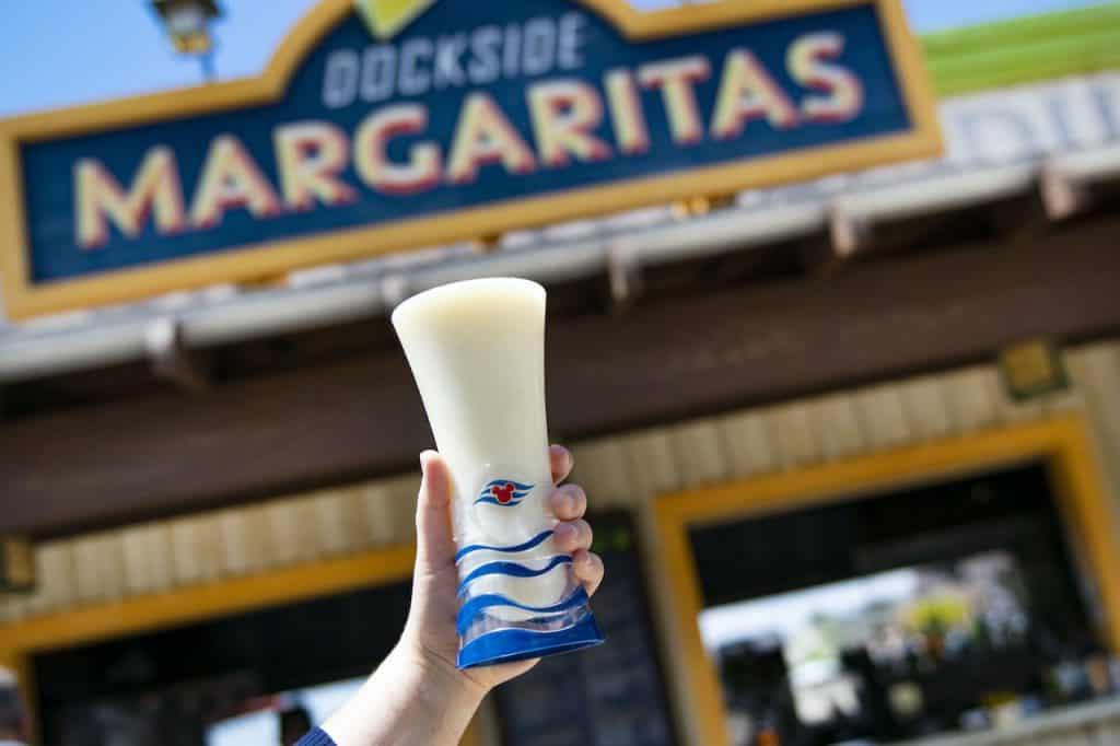 A refreshing frozen margarita is held up in front of the vibrant Dockside Margaritas sign at Disney Springs’ lively outdoor bar.