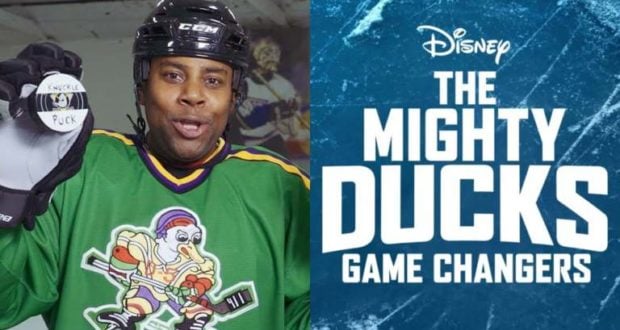 Kenan Thompson in a classic green Mighty Ducks hockey jersey holds a puck, standing next to "The Mighty Ducks: Game Changers" Disney logo, capturing the nostalgic energy of the beloved franchise for Disney fans.