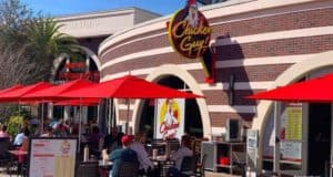 Guests enjoying outdoor seating beneath vibrant red umbrellas at Chicken Guy! in Disney Springs, soaking up the lively atmosphere and sunshine.