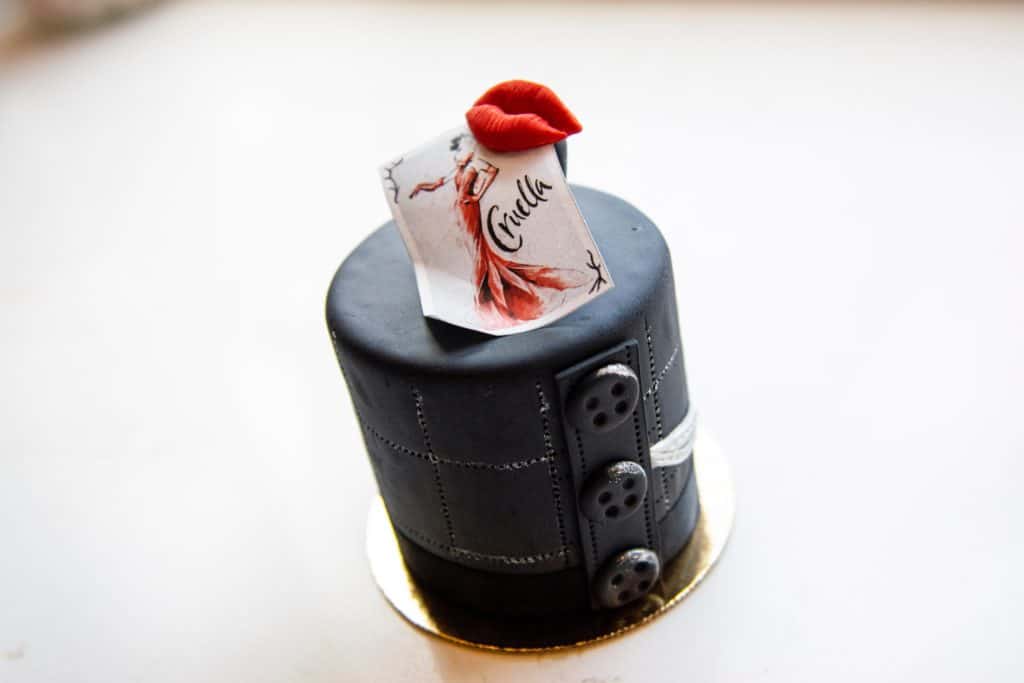 Cruella-inspired dessert at Disney Springs: a stylish black mini cake accented with button details, crowned by bold red lips and a "Cruella" card featuring her sketch—one of the latest arrivals for Disney fans to try.