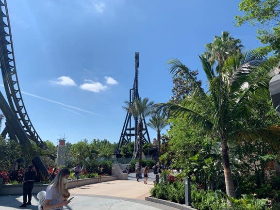 Guests stroll by the iconic VelociCoaster at Universal Orlando Resort, framed by lush palm trees and vibrant greenery under the Florida sun.