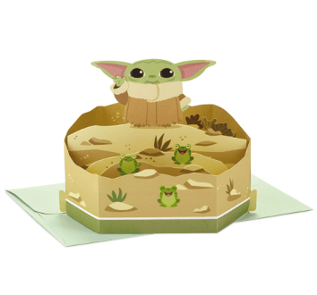 Pop-up 3D card featuring Grogu—known as The Child from Star Wars: The Mandalorian—with his signature big ears, joined by three playful frogs in a sandy Tatooine-inspired scene; an ideal keepsake for Star Wars fans and collectors, reminiscent of the fun found at Galaxy’s Edge.