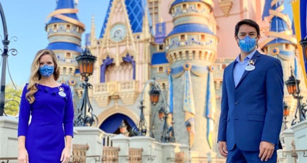 Disney Ambassadors in matching blue suits and face masks pose in front of Sleeping Beauty Castle at Disneyland, showcasing the magic and excitement of the park experience.