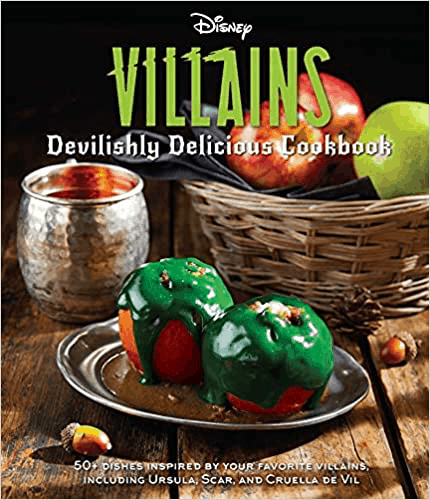 Disney Villains Cookbook cover on display, featuring eerie green-glazed apples and a bubbling sauce beside a glowing candle, with crisp apples set atop a rustic wooden table—inviting Disney Parks fans to relive the magic (and mischief) of their favorite villains through wickedly sweet recipes inspired by the parks' enchantment.