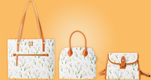 Three white floral handbags with tan straps and yellow accents from the Dooney & Bourke Disney Collection are artfully displayed on an orange backdrop, each bag highlighted by delicate Tinker Bell details perfect for Disney Parks fans seeking a touch of pixie dust magic in their accessory lineup.
