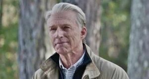 Old Man Steve from Avengers: Endgame poses outdoors in front of lush trees, dressed in his iconic beige jacket and checked shirt, just like when he appeared at the end of the film.