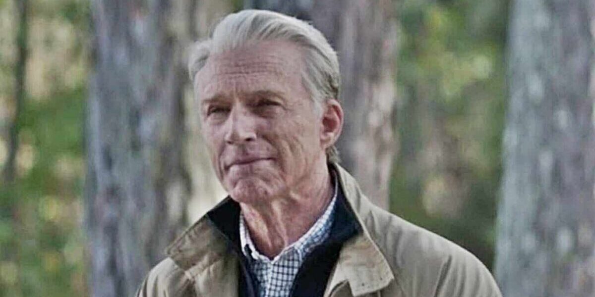 Old Man Steve from Avengers: Endgame poses outdoors in front of lush trees, dressed in his iconic beige jacket and checked shirt, just like when he appeared at the end of the film.