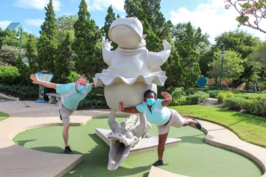 Guests strike playful poses beside the iconic bird statue at Fantasia Gardens Miniature Golf, basking in the sunny, vibrant scenery as the course marks 25 years of Disney magic and imaginative fun.