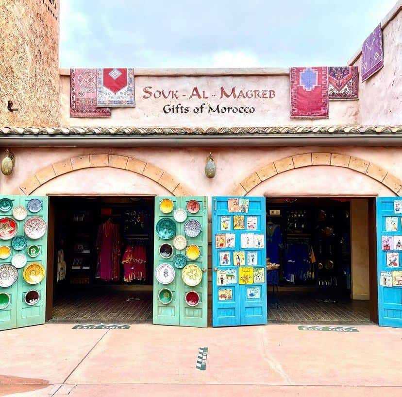The "Souk-Al-Magreb Gifts of Morocco" storefront at EPCOT’s Morocco Pavilion, featuring vibrant doors, decorative plates, and unique gifts, styled in the detailed and immersive tradition of Disney Imagineering.