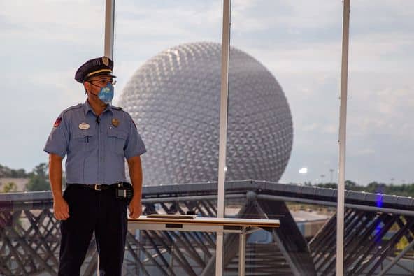 A masked security guard stands by the windows with Epcot’s iconic Spaceship Earth in the background, as a Cast Member gets ready to present the Disney Heroes Award.