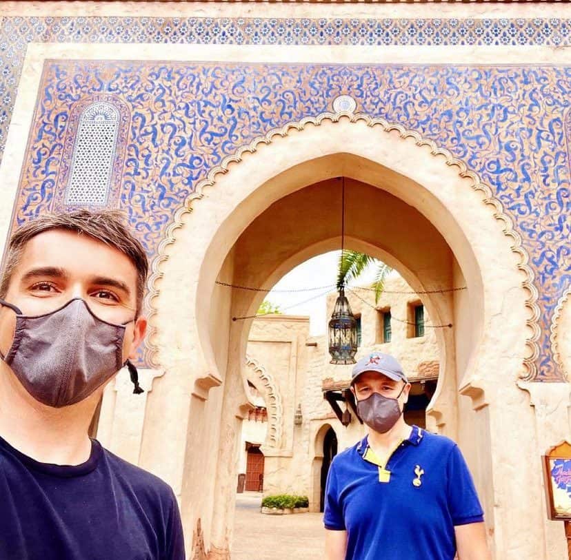 Guests at EPCOT’s Morocco Pavilion pose in front of the stunning blue-tiled archway, masks on, surrounded by intricate architectural details that highlight the pavilion’s authentic Moroccan ambiance.