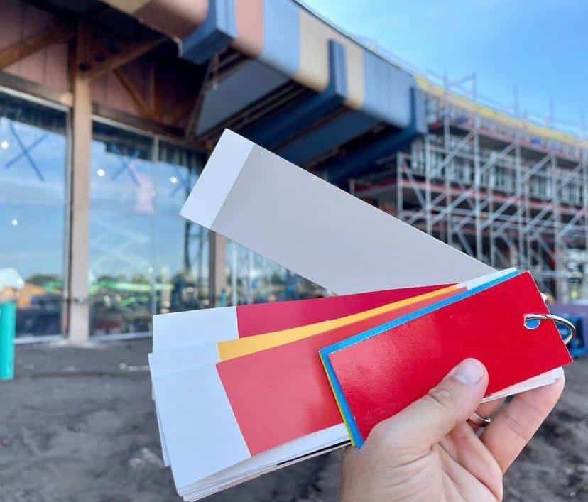 Color swatches are held up in front of a construction site with scaffolding at EPCOT, capturing the spirit of Disney Imagineering seen in projects like the Creations Shop.