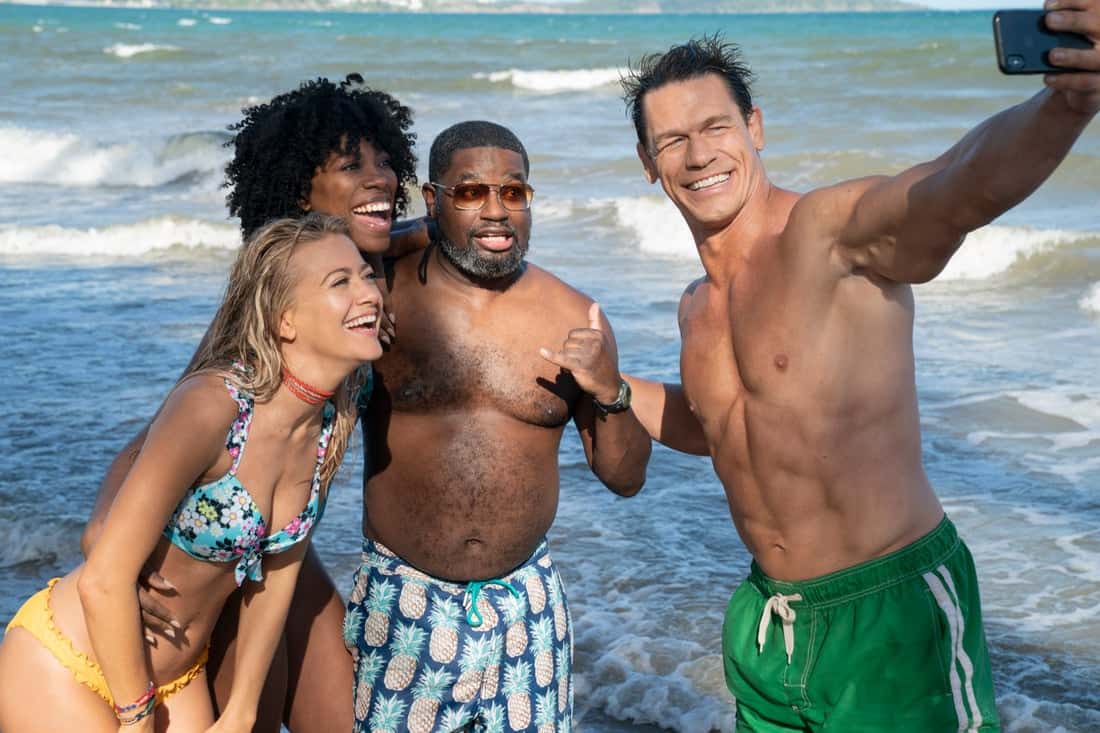 Four friends in colorful swimsuits strike a cheerful selfie on a sandy beach with ocean waves rolling behind them, capturing the fun and excitement of their vacation—just like guests making unforgettable memories together at a top entertainment resort.