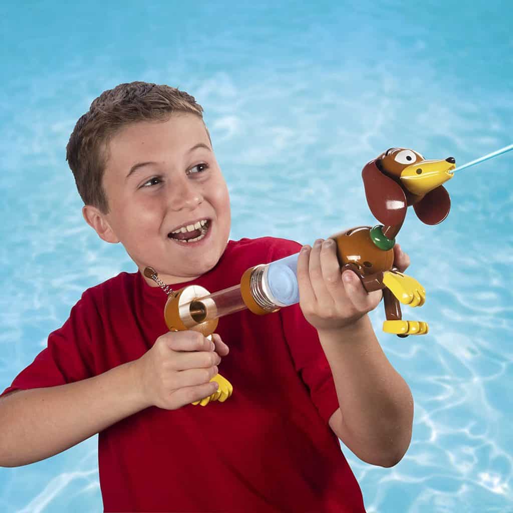 A young guest in a vibrant red shirt gleefully sprays water from a Slinky Dog Water Blaster beside the pool, experiencing Toy Story-themed fun with his latest Amazon discovery.
