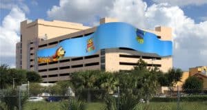 The International Drive parking garage features a colorful Toy Story Slinky Dog mural, set against a backdrop of lush trees and fencing, offering fans a lively Disney-themed photo spot just outside the parks.