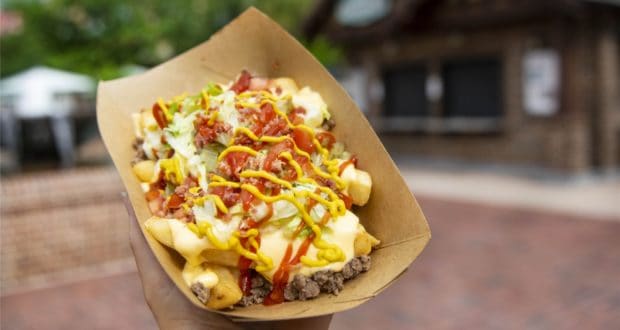 Cheeseburger Poutine served in a paper tray at Disney Springs, featuring crispy fries piled high with ground beef, melted cheese, lettuce, bacon pieces, ketchup, and mustard. This exclusive treat is available for a limited time for theme park guests to enjoy amidst the Disney Springs excitement.