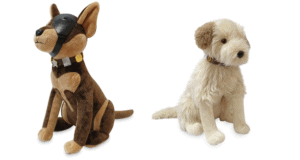 Wink and Buddy Plushes—beloved Pals from Universal Studios, one sporting a soft brown coat with a signature black mask and the other fluffy white—sit together against a crisp white backdrop, all set to charm guests with their signature theme park outfits.