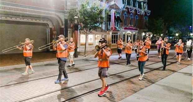 A vibrant marching band in bright orange vests energizes the nighttime parade route, filling the street with music and movement in true Disneyland Midnight Rehearsal fashion.