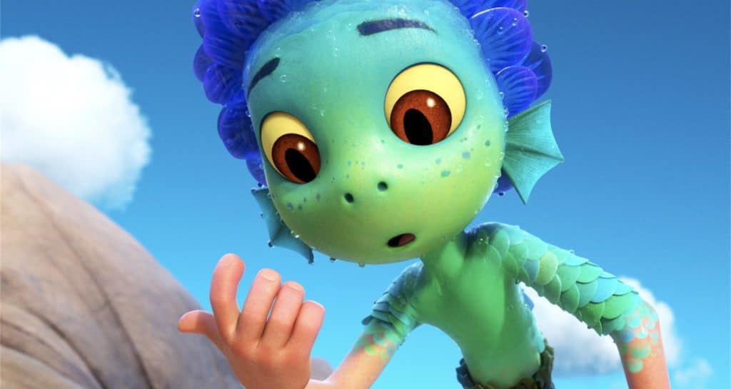 A wide-eyed, animated blue and green sea creature—reminiscent of the characters from Pixar’s "Luca"—strikes a surprised pose as it stares at its own hand under a vibrant blue sky, evoking the magic and wonder guests experience during character encounters at Pixar Pier.