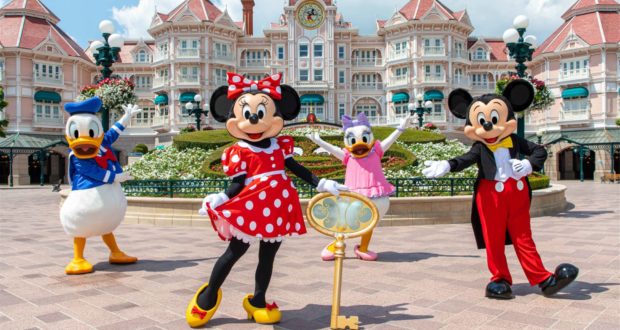 Mickey, Minnie, Donald, and Daisy joyfully pose with a golden key in front of Disneyland Paris’ iconic pink castle, marking the grand reopening and sharing the excitement of magical new experiences with guests.
