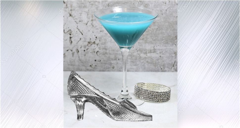 The Glass Slipper Martini—a dazzling blue cocktail served in a martini glass—sits beside a sparkling Cinderella slipper and a shimmering silver bracelet on a pale surface, set against a soft gray backdrop to evoke the enchanting magic of Disney Parks.
