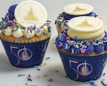 Celebratory cupcakes topped with swirls of purple and white frosting, festive sprinkles, and shimmering Walt Disney World 50th Anniversary emblems—perfect treats found at the parks during the milestone celebration.