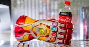 The iconic Infinity Gauntlet, gleaming in red and gold, proudly clutches a Coca-Cola bottle as its vibrant stones shimmer—like you’ve caught Iron Man himself at Avengers Campus, taking a refreshment break between heroic moments.