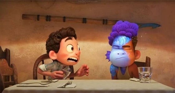 At Pixar Pier, two animated boys share a table, capturing a magical Luca moment—one is wide-eyed in awe as his friend’s face fantastically shifts with vibrant blue scales, echoing the film’s signature transformation scene.