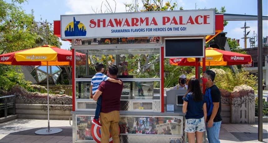 Guests line up at the Shawarma Palace food stand, marked by a Marvel superhero-themed sign with Iron Man and Infinity Gauntlet references. Bright umbrellas add to the immersive Disney California Adventure vibe, bringing favorite Avengers moments and flavors to life.