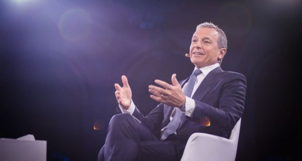 Disney Chairman Bob Iger, dressed in a suit and seated on a white chair beneath bright stage lights, addresses an audience with a headset microphone as he shares insights about the future of Disney’s entertainment offerings and company strategy.