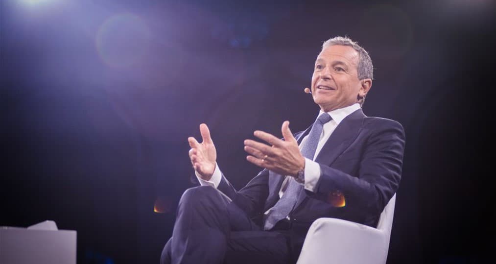 Disney Chairman Bob Iger, dressed in a suit and seated on a white chair beneath bright stage lights, addresses an audience with a headset microphone as he shares insights about the future of Disney’s entertainment offerings and company strategy.