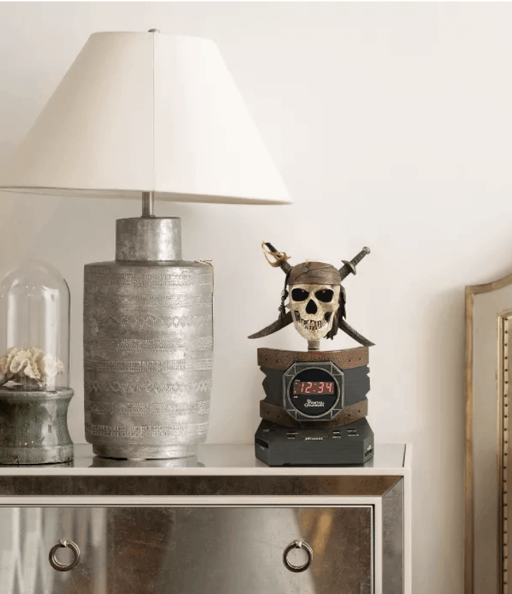 A Pirates of the Caribbean alarm clock featuring iconic Disney theming and a stylish lamp rest atop a metallic nightstand, bringing a touch of magic and adventure to this modern, Disney-inspired room.