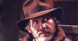 Indiana Jones, wearing his iconic brown hat and jacket, stands with a serious expression and a hint of adventure in his eyes, channeling the classic look seen in Indiana Jones 5.