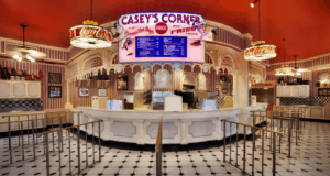 Step into Casey’s Corner, the beloved Magic Kingdom eatery where retro vibes meet Disney nostalgia—complete with a curved counter, illuminated menu board, bright red ceiling, and classic Coca-Cola signs—now welcoming guests once again after its highly anticipated reopening.