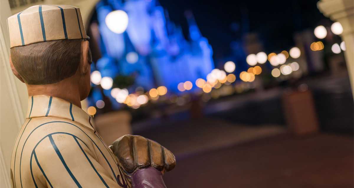 Mickey Mouse, dressed in his classic striped uniform, stands proudly facing the glowing Magic Kingdom castle at night, as the park buzzes with excitement and enchantment for the grand reopening celebration.