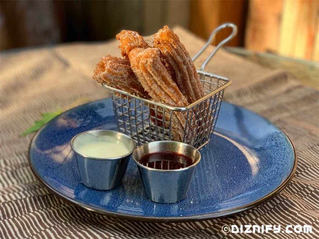 Gluten-free churros served in a metal basket with two dipping sauces on a blue plate, ready to enjoy as a tasty treat during your Walt Disney World adventure.
