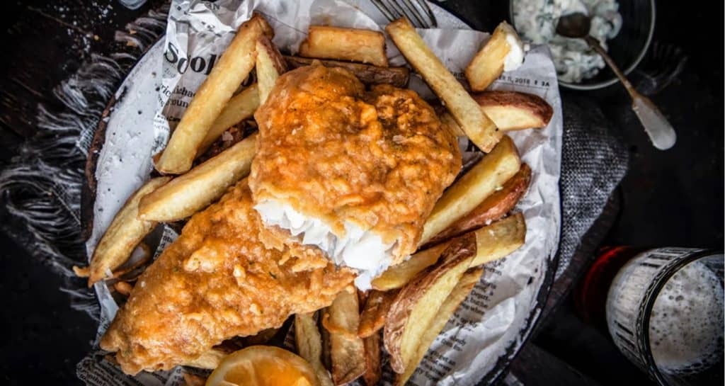Crispy golden fish and thick-cut fries rest on a sheet of newspaper, garnished with a lemon wedge and accompanied by dipping sauce—one of the beloved gluten-free classics guests can savor at Walt Disney World.
