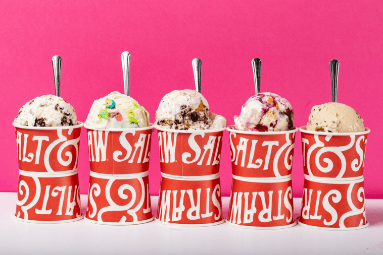 Five colorful scoops of ice cream in red Salt & Straw cups, set out in a playful row with spoons ready, bring the fun and flavor of Disney Springs' popular ice cream spot to life against a vibrant pink backdrop.