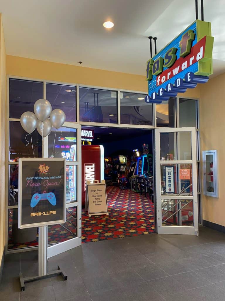 The entrance to the Fast Forward arcade, featuring vibrant arcade games, festive balloons, and a prominently displayed sign listing hours of operation, capturing the energetic vibe reminiscent of Disney World’s signature arcades.