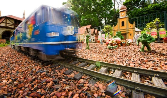 A vibrant blue toy train zips through a detailed miniature landscape filled with tiny buildings and guests, capturing the playful spirit and storytelling magic of EPCOT’s iconic model railway displays.