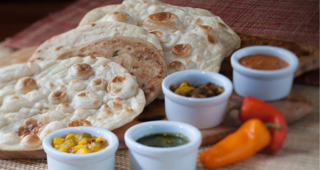 Gluten free naan bread served with an array of flavorful dips and sauces in small bowls, plus two vibrant peppers on the side—an Instagram-worthy snack option you’ll find at Walt Disney World, perfect for foodies exploring the parks.