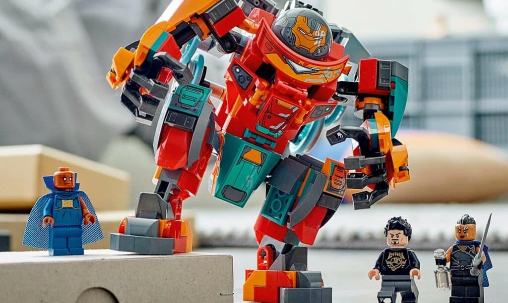 Tony Stark in his Sakaarian Iron Man suit teams up with two other LEGO minifigures beside a vibrant, oversized LEGO mech, ready for action like a hero meet-and-greet at LEGOLAND’s interactive build zone.