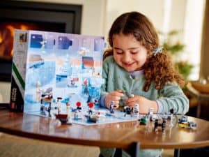 A young Star Wars fan opens The Mandalorian-themed LEGO advent calendar at a table, eagerly playing with collectible mini-figures just like those found at a Star Wars attraction in a theme park.